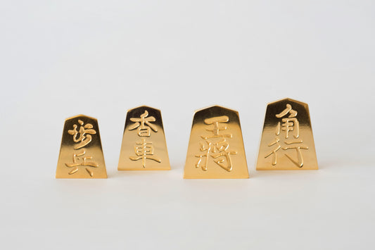 極み 削ることの極 磨き上げる極 一つひとつ職人による手作りでお届けします 24金が美しい将棋駒 実寸大のサイズで作られた、スチールに24金メッキ加工を 施した将棋駒です。精密加工機により実現された精巧な仕上がりで 手作業にて丁寧にっ磨き上げられるからこそ輝く光沢と 滑らかな手触りです。縁起物、インテリア、贈り物、景品としても ご利用いただけます。 駒の大きさは一般的なものと同じですが、 王将の大きさですと35gの重さがあります。 金属ならではの重厚感をお楽しみいただけます。 洗練されたデザインの化粧箱付きです。 購入後、そのままプレゼントしていただけます。 愛好家の方や、ちょっと変わったものが好きな方へのギフトとして おすすめです。大会の景品としても人気です。 高級感のあるインテリアとしてお楽しみいただけます。 # 藤井聡太 さん # 藤井聡太竜王名人 #  藤井聡太八冠