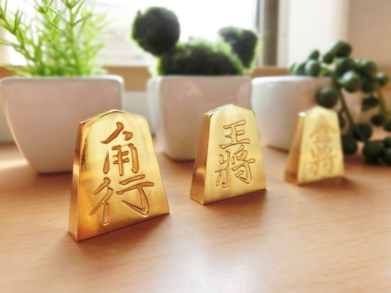 極み 削ることの極 磨き上げる極 一つひとつ職人による手作りでお届けします 24金が美しい将棋駒 実寸大のサイズで作られた、スチールに24金メッキ加工を 施した将棋駒です。精密加工機により実現された精巧な仕上がりで 手作業にて丁寧にっ磨き上げられるからこそ輝く光沢と 滑らかな手触りです。縁起物、インテリア、贈り物、景品としても ご利用いただけます。 駒の大きさは一般的なものと同じですが、 王将の大きさですと35gの重さがあります。 金属ならではの重厚感をお楽しみいただけます。 洗練されたデザインの化粧箱付きです。 購入後、そのままプレゼントしていただけます。 愛好家の方や、ちょっと変わったものが好きな方へのギフトとして おすすめです。大会の景品としても人気です。 高級感のあるインテリアとしてお楽しみいただけます。 # 藤井聡太 さん # 藤井聡太竜王名人 # 藤井聡太八冠
