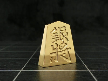 極み　削ることの極　磨き上げる極 一つひとつ職人による手作りでお届けします 24金が美しい将棋駒 実寸大のサイズで作られた、スチールに24金メッキ加工を 施した将棋駒です。精密加工機により実現された精巧な仕上がりで 手作業にて丁寧にっ磨き上げられるからこそ輝く光沢と 滑らかな手触りです。縁起物、インテリア、贈り物、景品としても ご利用いただけます。 駒の大きさは一般的なものと同じですが、 王将の大きさですと35ｇの重さがあります。 金属ならではの重厚感をお楽しみいただけます。 洗練されたデザインの化粧箱付きです。 購入後、そのままプレゼントしていただけます。 愛好家の方や、ちょっと変わったものが好きな方へのギフトとして おすすめです。大会の景品としても人気です。 高級感のあるインテリアとしてお楽しみいただけます。 ＃ 藤井聡太 さん　＃ 藤井聡太竜王名人　＃　藤井聡太八冠